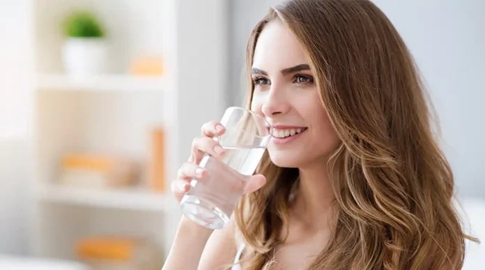 Remedios naturales para tratar los sofocos en la menopausia Una mujer madura sonriendo mientras bebe un vaso de agua, ilustrando cómo tratar los sofocos en la menopausia con hábitos saludables.